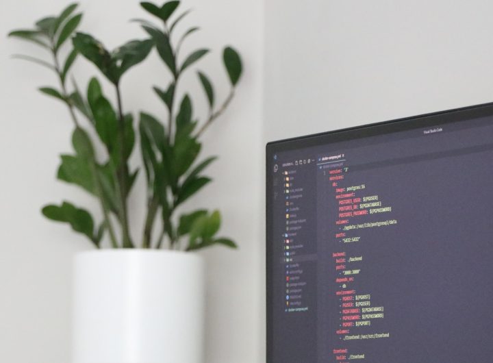 A computer monitor sitting on top of a desk next to a plant