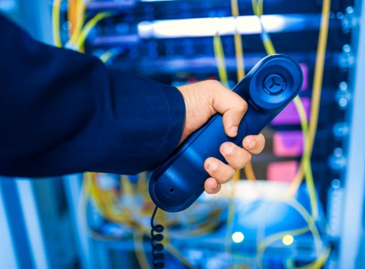 Close-up of a hand holding a telephone receiver in a server room emphasizing technology.